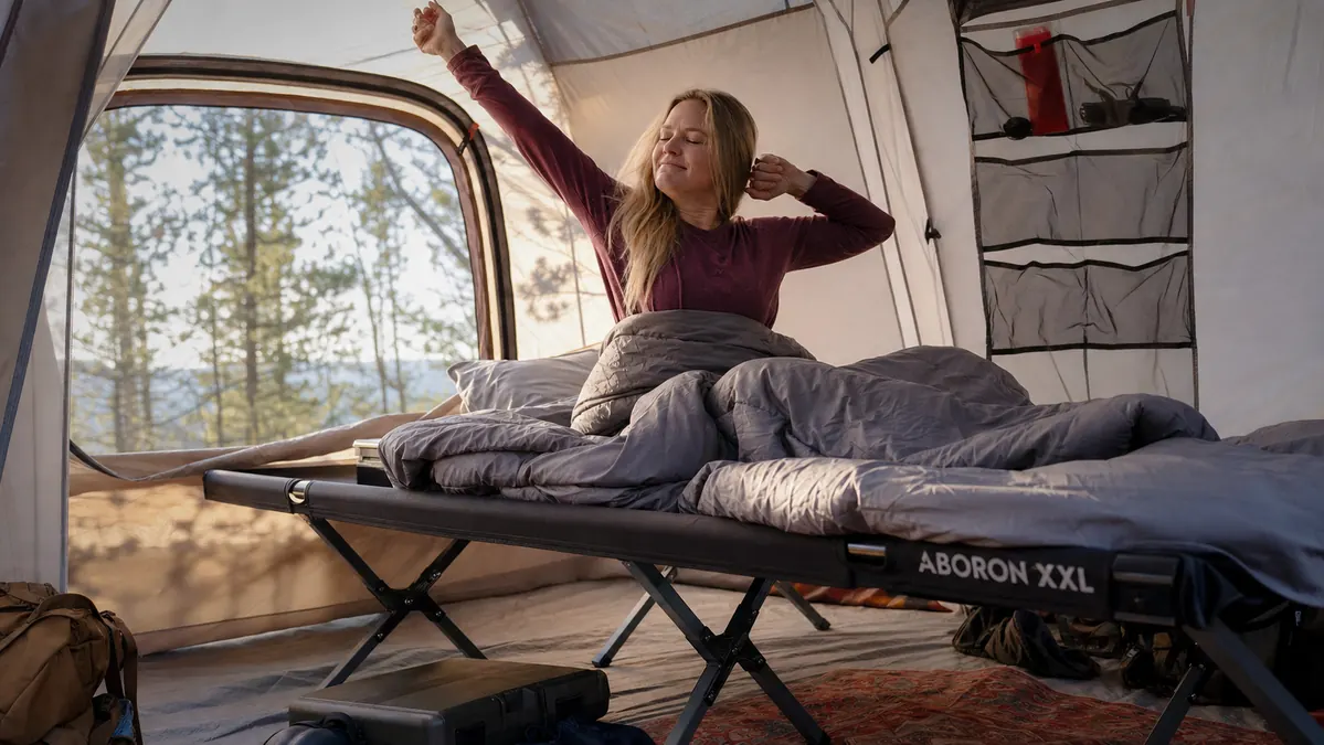 Camper waking up on the ABORON XXL camping cot inside a tent at sunrise