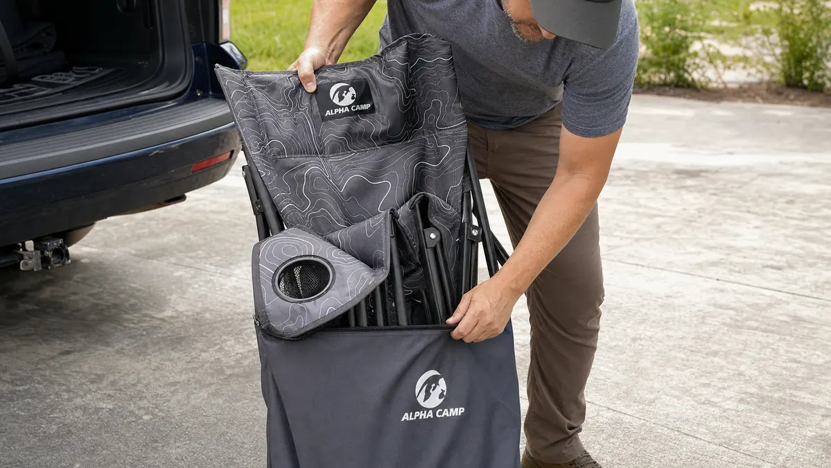 Close-up of hands wrestling the ALPHA CAMP chair back into its carry bag on a driveway