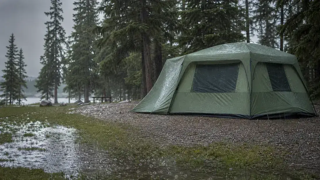 A family cabin tent pitched on a slight rise with rain falling around it, rainfly fully staked out